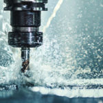 Closeup shot of a CNC machine processing a piece of metal. There are three water streams splashing the object to cool it down.